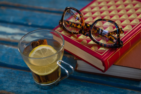 Close up of lemon tea by books and eyeglasses on wooden table