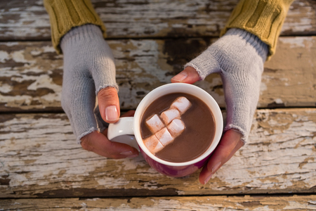 Cropped  hand of woman having hot chocolate at wooden tableの写真素材