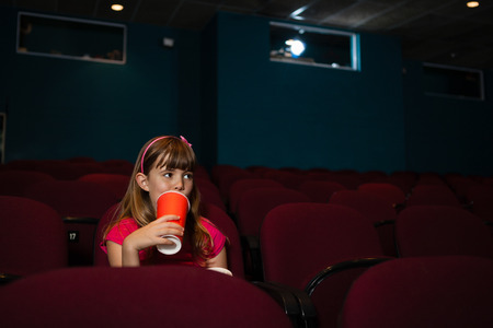 Girl having drink while sitting on seat in movie theaterの写真素材