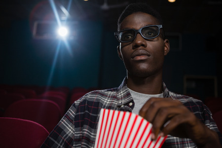 Concentrated man having popcorn while watching movie in theatreの写真素材
