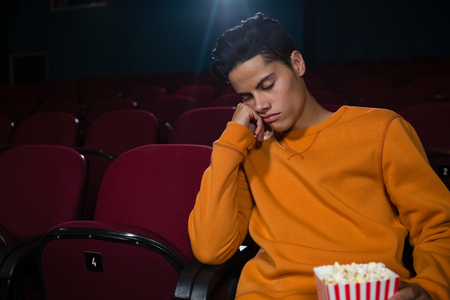 Bored man with popcorn sleeping in theatreの写真素材