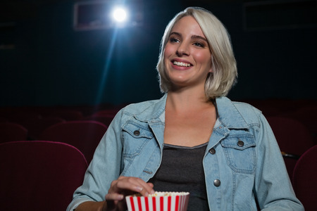 Happy woman having popcorn while watching movie in theatreの写真素材