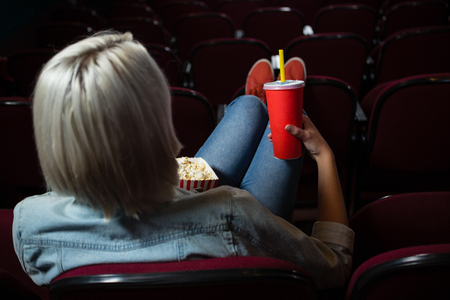 Rear view of woman having drinks while watching movie in theatreの写真素材
