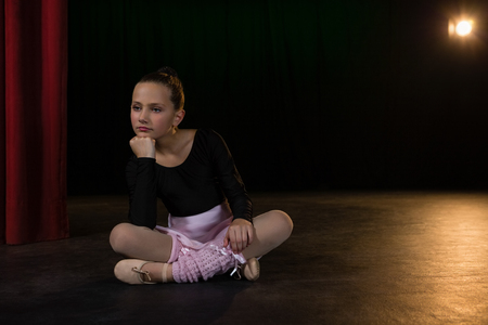 Thoughtful ballerina sitting on the stage in theatreの写真素材