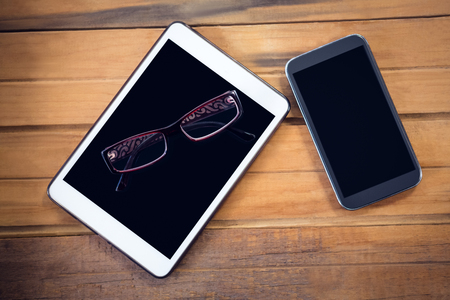 Overhead view of digital tablet with smartphone and eyeglasses on wooden tableの写真素材
