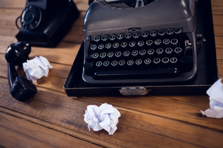 High angle view of typewriter by telephone and crumpled papers on wooden table