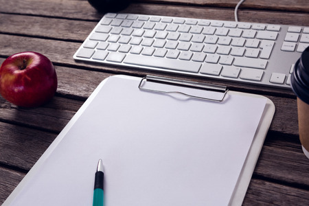 Close-up of keyboard, clipboard, apple and pen on wooden tableの写真素材