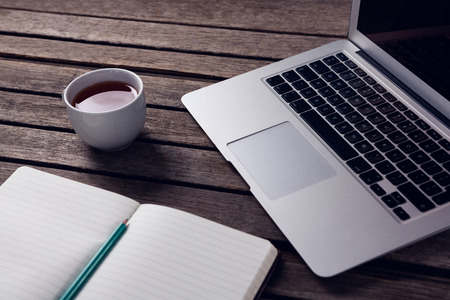 Close-up of laptop, black coffee and diary on wooden tableの写真素材