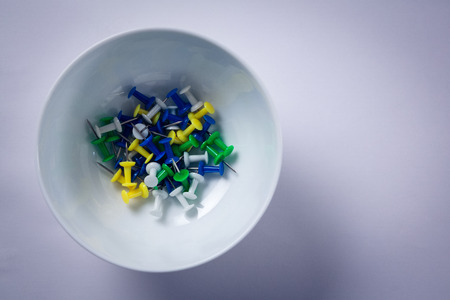 Overhead of various push pins in bowl on white background