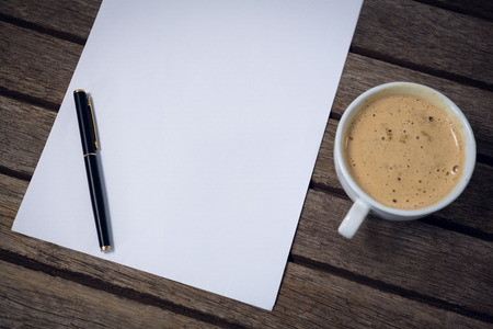 High angle view of coffee cup with paper and fountain pen on wooden tableの写真素材
