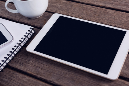 Overhead of digital tablet, mobile phone, black coffee and diary on wooden tableの写真素材