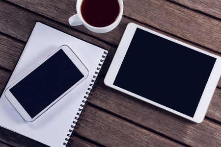 Overhead of digital tablet, mobile phone, black coffee and diary on wooden table
