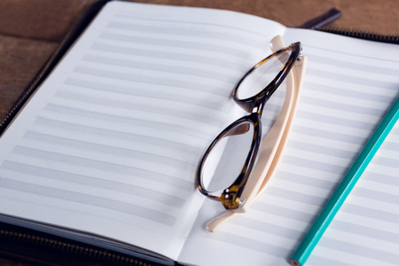 Close-up of spectacles and pencil on organizer at tableの写真素材