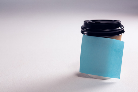 Close-up of disposable glass with blank sticky note on white backgroundの写真素材