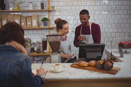 Male owner with woman using diigital tablet while standing in cafeの写真素材