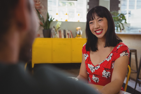 Happy young woman looking at boyfriend while sitting in cafeの写真素材