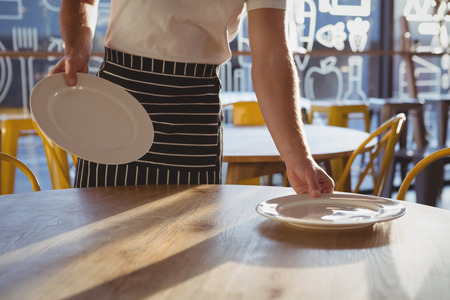 Mid section of waiter arranging plates on wooden table at cafeの写真素材