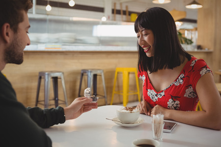 Young man gifting ring to happy girlfriend in cafeの写真素材