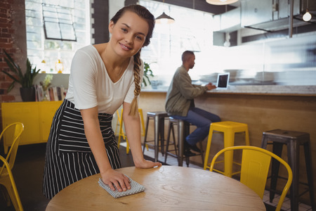 Portrait of young waitress cleaning table at cafeの写真素材