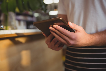 Midsection of waiter using digital tablet by counter in cafeの写真素材