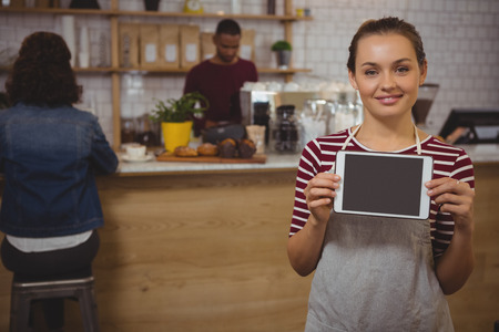 Portrait of female owner with digital tablet standing at cafeの写真素材