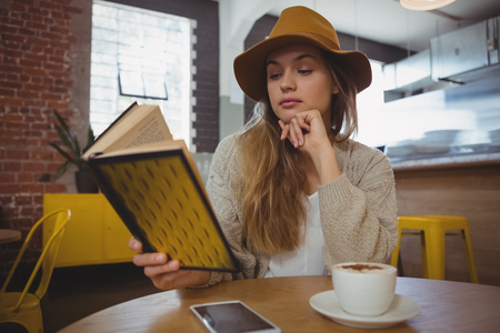 Young woman reading book at table in cafeの写真素材