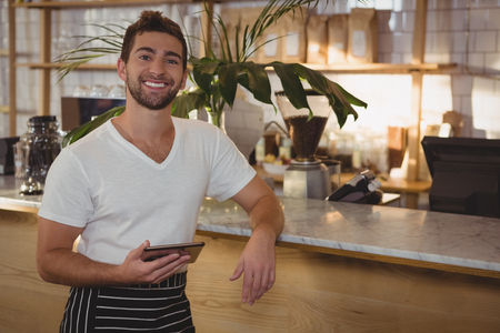 Portrait of waiter with digital tablet standing by counter at cafeの写真素材