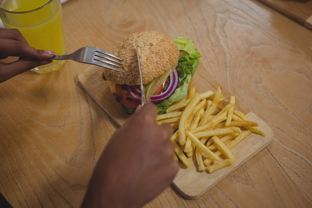 Cropped hands of man having burger and French fries at wooden table in cafe