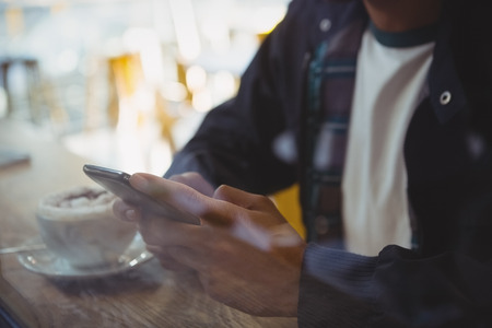 Mid section of man with coffee using phone seen through glass in cafeの写真素材
