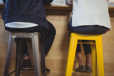 Low section of couple sitting on stools at counter in cafeの写真素材
