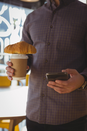 Mid section of businessman using phone while having coffee in cafeの写真素材