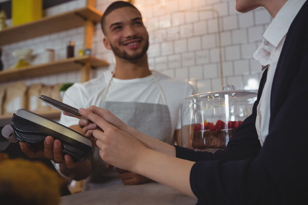 Waiter showing credit card reader to female owner at counter in cafeの写真素材