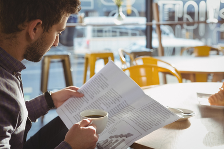 Young businessman having coffee while reading newspaper in cafeの写真素材
