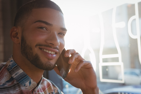 Portrait of smiling young man talking on mobile phone in cafeの写真素材