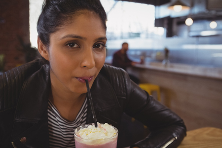 Portrait of young woman drinking milkshake at cafeの写真素材