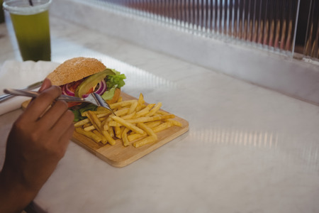 Cropped hand of woman having French fries and burger at counter in cafe