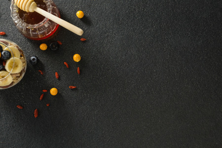Honey dipper with cup of yogurt muesli, banana and blueberries for breakfast on black backgroundの写真素材
