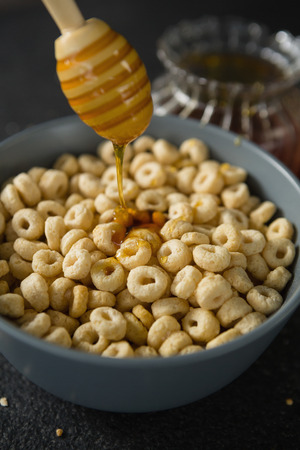 Honey being poured in bowl of cereal rings on black backgroundの写真素材