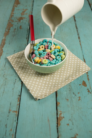 Milk being pour into glass of cereal rings on wooden tableの写真素材