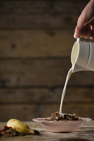 Close-up of hand pouring milk on wheat flakesの写真素材