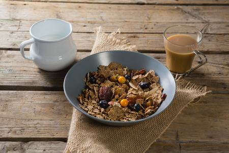 Bowl of wheat flakes, blueberry and golden berry with milk jug on tableの写真素材