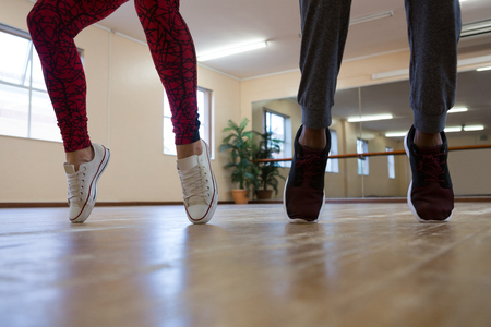 Low section of woman with friend practicing dance on floor in studioの写真素材