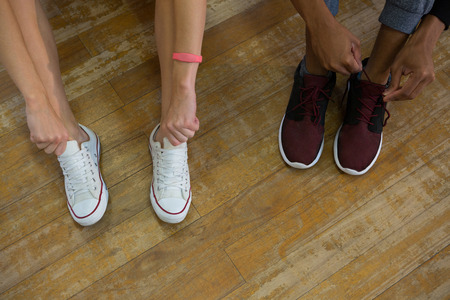 Low section of dancers tying shoelaces on wooden floor at studioの写真素材