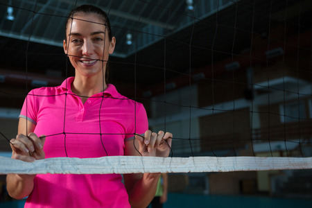 Portrait of smiling female volleyball player standing behind netの写真素材