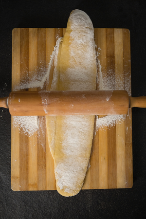 Directly above shot of rolling pin on dough over cutting board at table