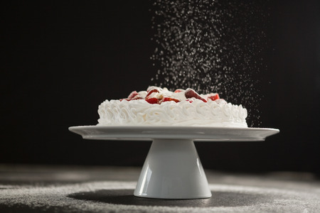 Powdered sugar falling over white cake on stand against black background