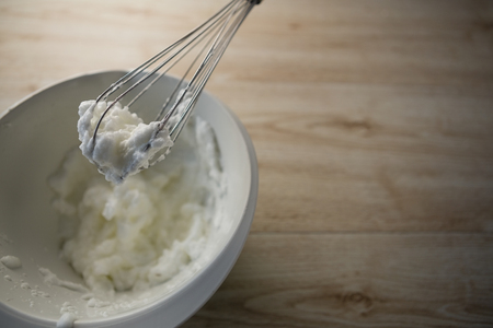 High angle view of wire whisk with whipped cream on bowl at tableの写真素材