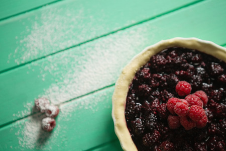 Raspberries and blackberries on tart in baking pan at tableの写真素材