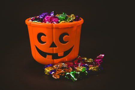 Bucket with colorful wrapped chocolates during Halloween over black backgroundの写真素材