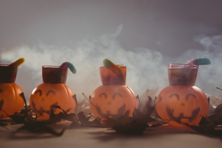 Food in jack o lantern containers with autumn leaves on table during Halloweenの写真素材